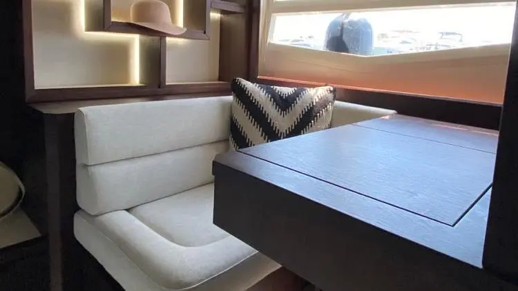 Stylish boat interior with a beige seat, decorative shelving, and a window view, featuring a decorative hat and cushion.